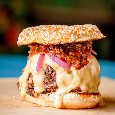 Brisket queso sandwich topped with meat sauce and served on a sesame bun.