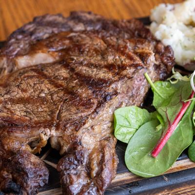 Grilled ribeye steak served with mashed potatoes and greens.