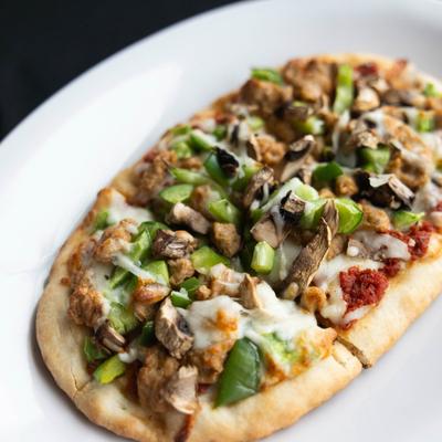 Flatbread topped with green bell peppers, mushrooms, melted cheese, and meat.