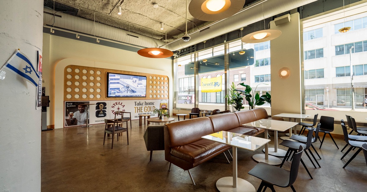 Interior of a modern café with a brown leather banquette, white tables, and black chairs