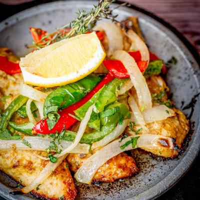 Pan-seared chicken topped with bell peppers, onions, lemon wedge, and thyme.