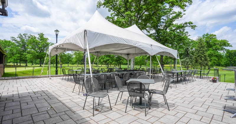 Outdoor area, white canopy tent, tables and chairs on a stone courtyard, surrounded by greenery