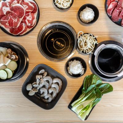 Various types of broths in a pots, raw shrimp and clams, sliced meat and other ingredients.