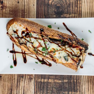 Sandwich on a sesame seed baguette, topped with melted cheese and a balsamic glaze.