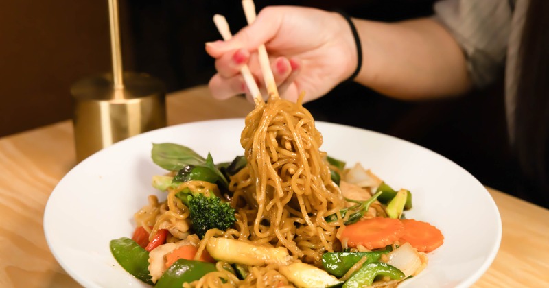 Stir-fried egg noodles being lifted from the plate with chopsticks