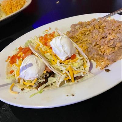 Beef tacos, topped with lettuce, cheese, tomato, sour cream, served with rice and beans.