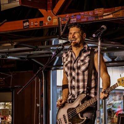 Bass guitarist standing in front of a microphone, holding the bass and smiling.
