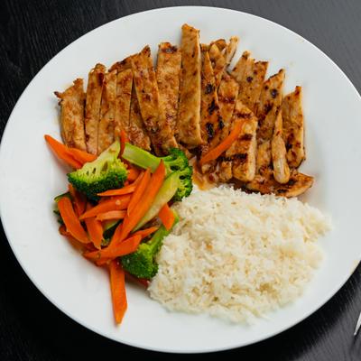 Sliced grilled chicken served with rice, broccoli, and carrots.