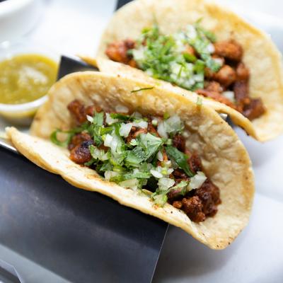Al pastor tacos topped with chopped onion and cilantro.