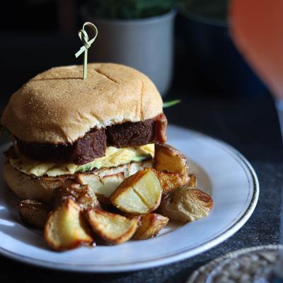 A sandwich with corned beef, scrambled egg, and caramelized onions, served with potatoes.