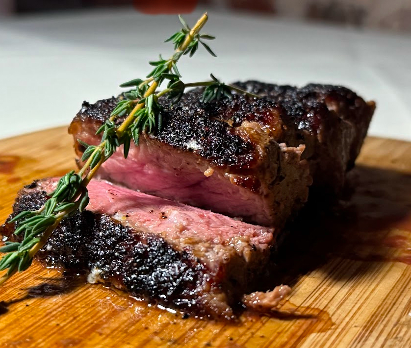 sliced, juicy, medium rare strip steak, with a rosemary sprig