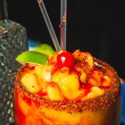 Mangonada cocktail, with spiced rim, garnished with cherry and lime, extreme close up.