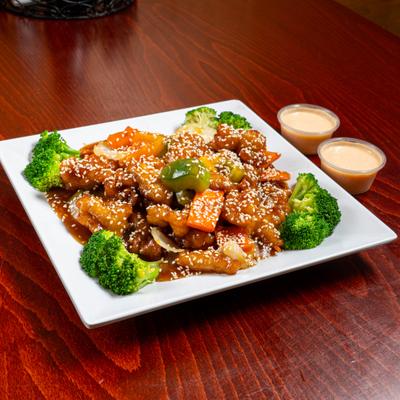 Sesame chicken plate served with two cups of dipping sauce on a wooden table.
