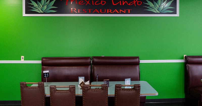 A restaurant table with brown leather chairs in front of green wall with "Mexico Lindo" sign