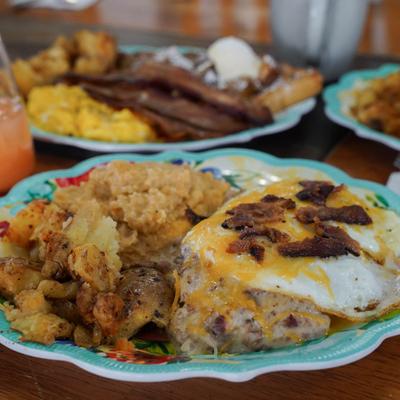 A breakfast plate featuring fried eggs, bacon, grits, and seasoned potatoes.