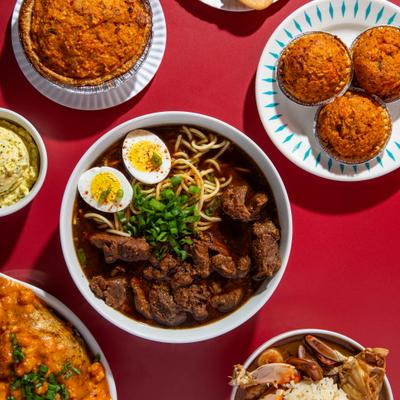 Beef noodle soup with eggs and herbs surrounded by assorted dishes.