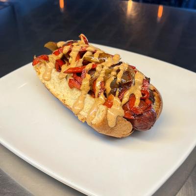 Hot dog topped with peppers onions and creamy sauce.