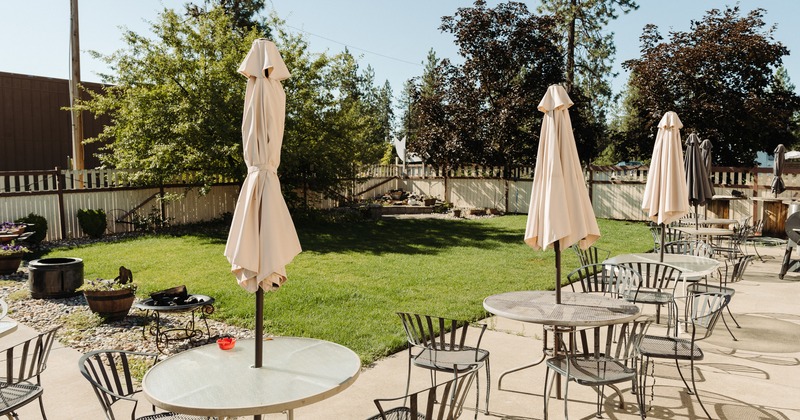 Outdoor patio featuring tables, parasols, and chairs on concrete, and a lawn area