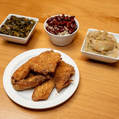 Fried tilapia served with collard greens, red beans and rice, and cabbage.