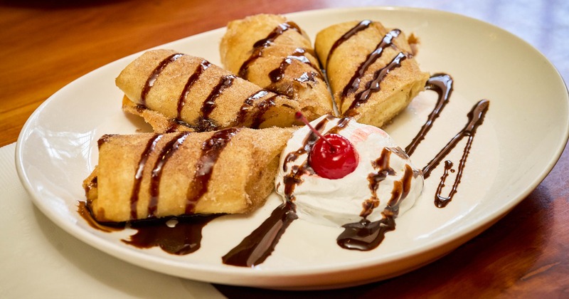Fried cheesecake chimichangas drizzled with chocolate sauce, served with whipped cream and cherry