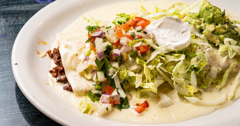 Chimichanga topped with lettuce, tomatoes, guacamole, and sour cream