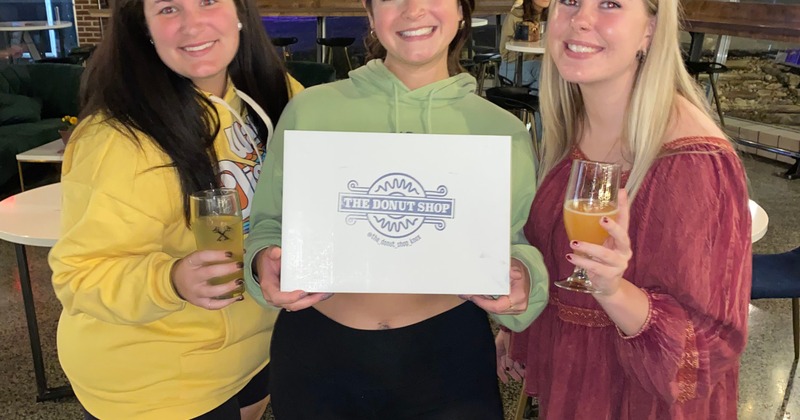 Three customers posing with The Donut shop delivery box