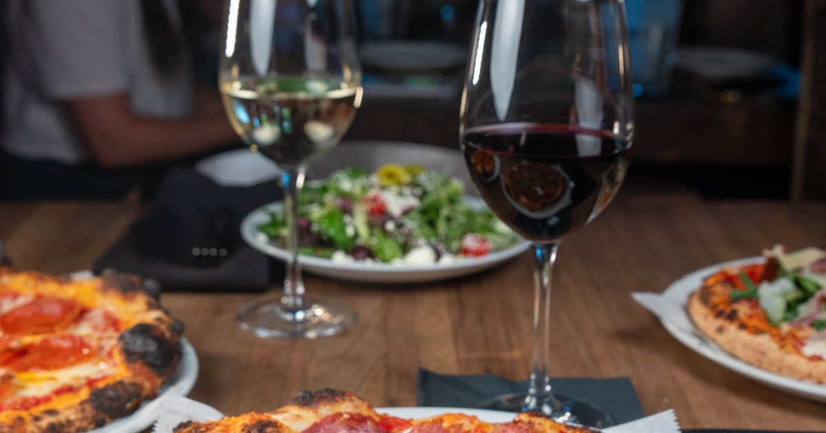 Various pizzas and glasses of wine on a table