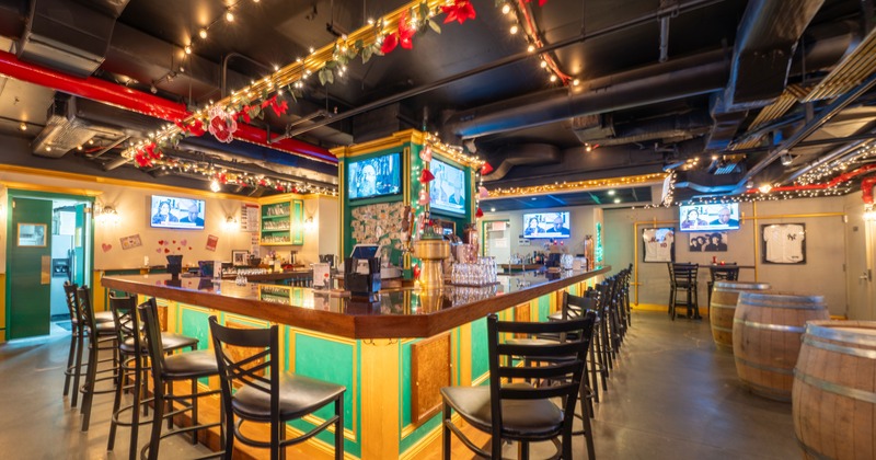 Interior of a cozy sports bar with a large, square-shaped bar counter and black bar stools