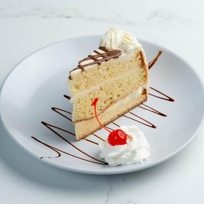 Tres leches cake with whipped cream, chocolate drizzle, and maraschino cherry garnish.