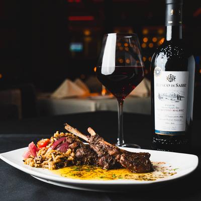 Roasted lamb chops with rice and vegetables, accompanied by red wine.