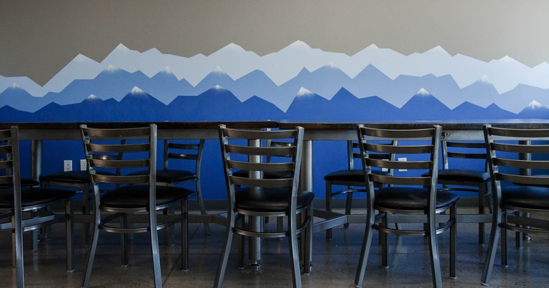 Interior, lined up tables and chairs, by a wall mural