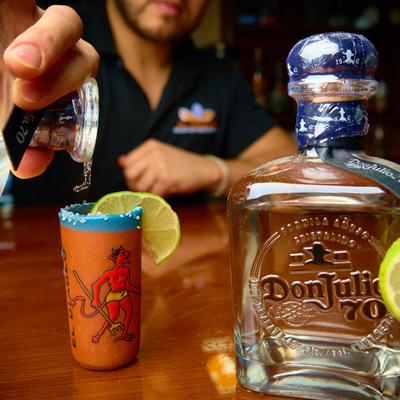 A bartender pouring  tequila into a shot glass next to a tequila bottle.