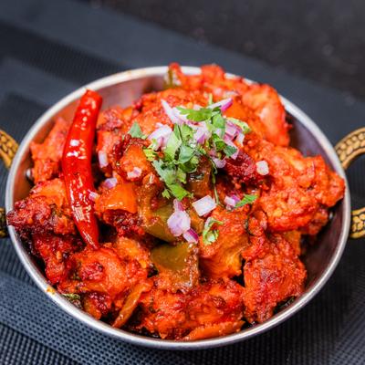Chili chicken garnished with onions and herbs.