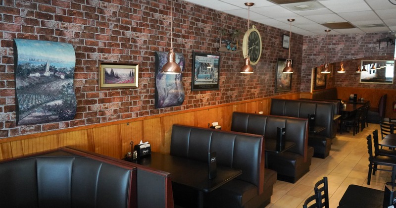 A cozy restaurant interior with a rustic brick wall, featuring black leather booths, copper pendant lights