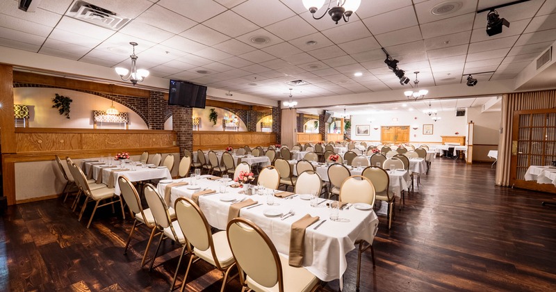 A large banquet hall with arranged tables covered in white tablecloths