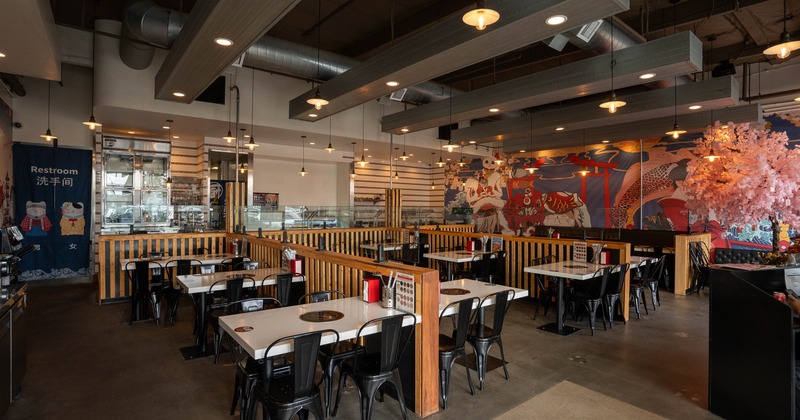 A modern Asian-themed restaurant with tables, black chairs, a mural and a pink cherry blossom tree