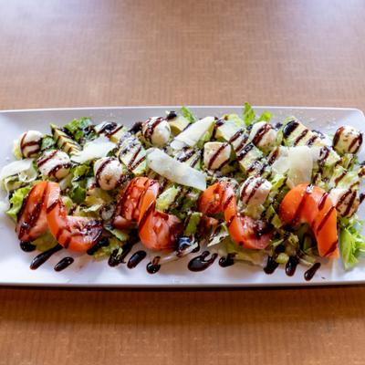 Avocado caprese salad with lettuce, tomatoes, mozzarella, Parmesan, and balsamic drizzle.