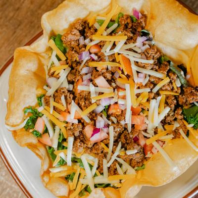 Taco Salad featuring ground beef and shredded cheese served in a fried tortilla bowl.