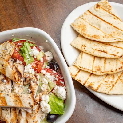Greek salad topped with grilled chicken, served with pita on the side.
