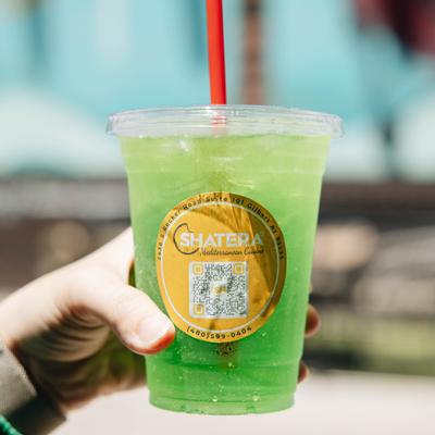 Hand holding a green iced drink served in a branded plastic cup.