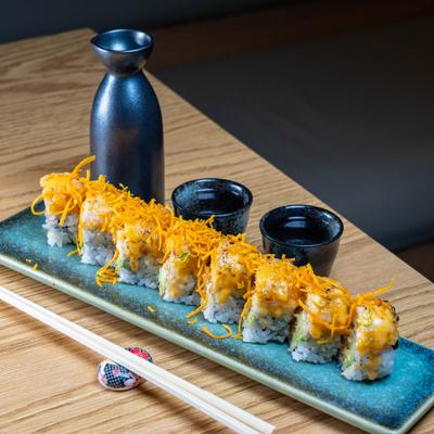Spicy Ocean Roll arranged on a rectangular platter next to small cups and a sake bottle.