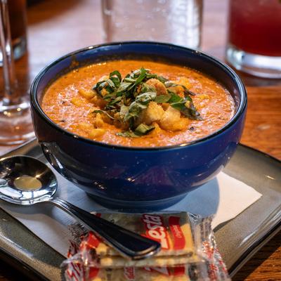 A bowl of tomato bisque served with crackers and garnished with herbs.