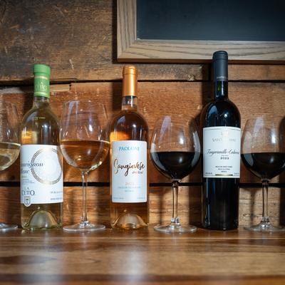 Three bottles of wine and four glasses of wine against a wooden wall.