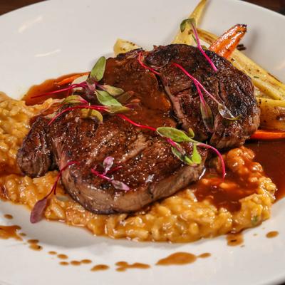 Seared beef steak served over a bed of creamy risotto with a side of roasted vegetables.