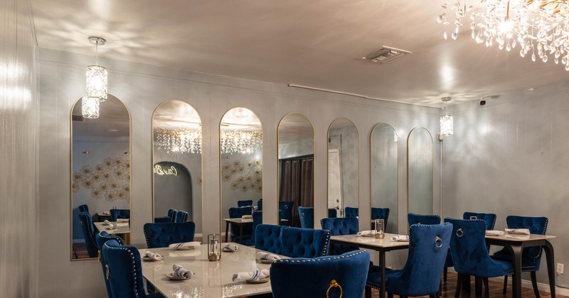 Elegant dining room with velvet blue chairs, marble tables and arched mirrors.