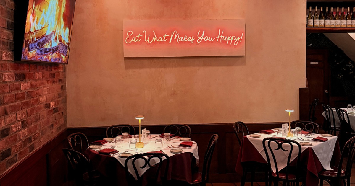 Dining tables beneath a neon sign reading Eat What Makes You Happy