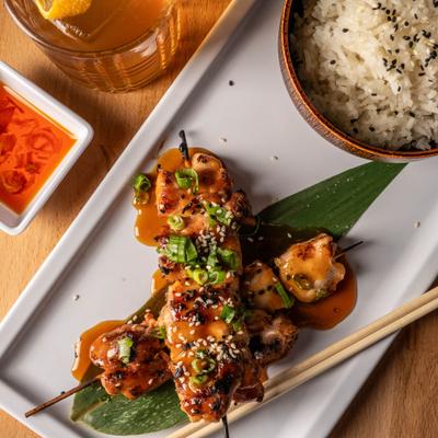 Grilled skewered chicken served with sides of white rice, dipping sauce and a cocktail.