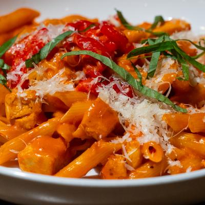 Penne Alla Vodka topped with grated parmesan cheese and fresh basil leaves.