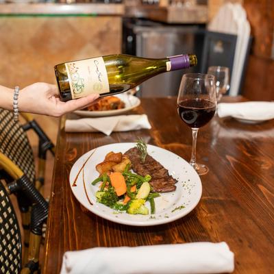 Red wine is being poured into a glass on a table with served meals.