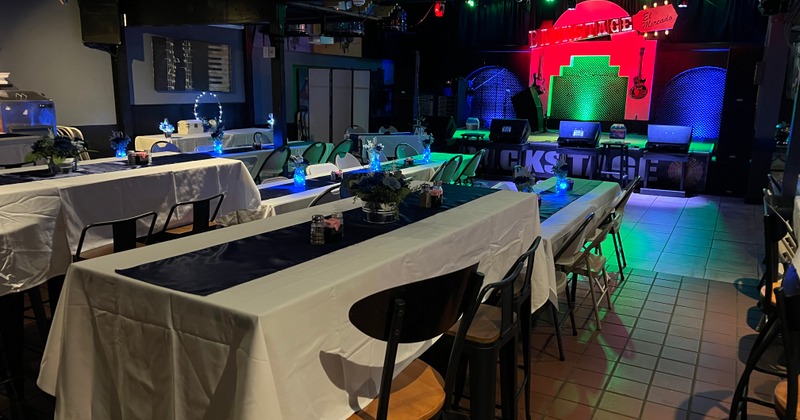 Dimly lit event space with long tables, A stage in the background displays colorful lights